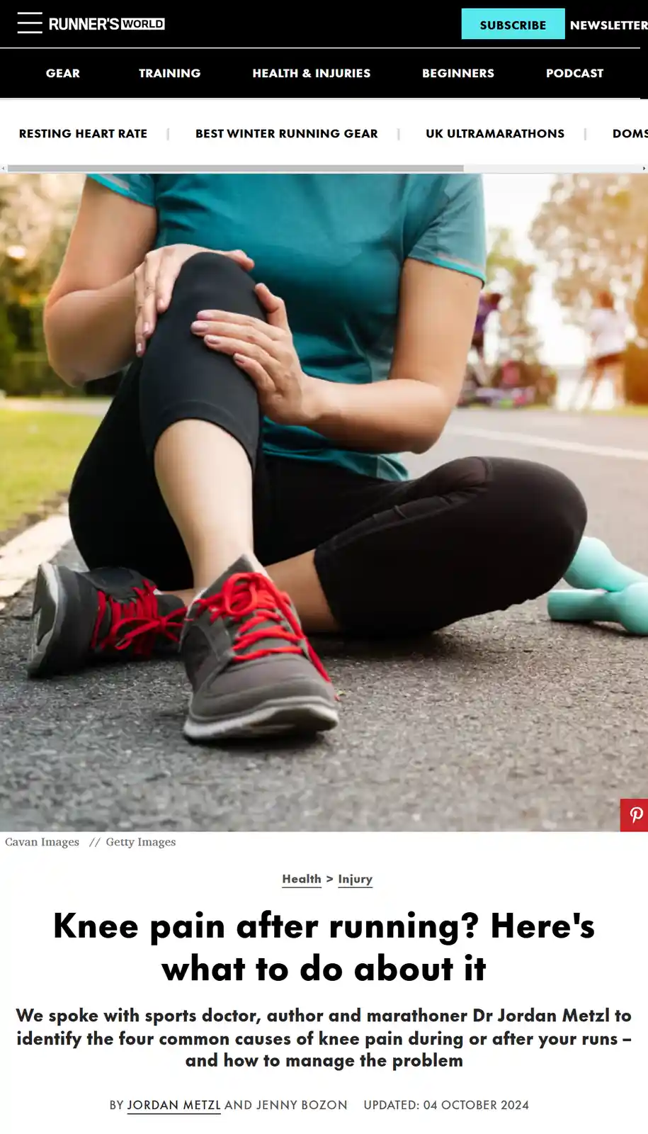 A woman in athletic wear is sitting on a paved path, holding her knee with both hands, appearing to be in pain. She wears a…