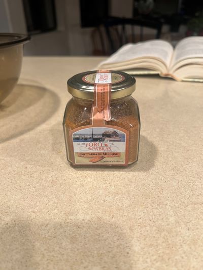 A small glass jar of 'Toro & Sapore' brand 'Butter Garlic & Rosemary' seasoning sits on a kitchen counter, with an open book…