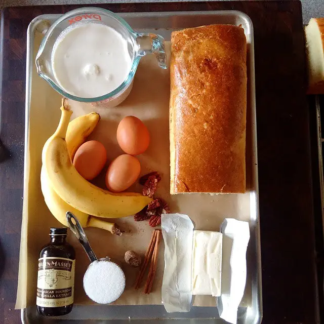 An overhead shot of ingredients for banana bread on a baking tray, including bananas, eggs, milk, butter, sugar, vanilla…