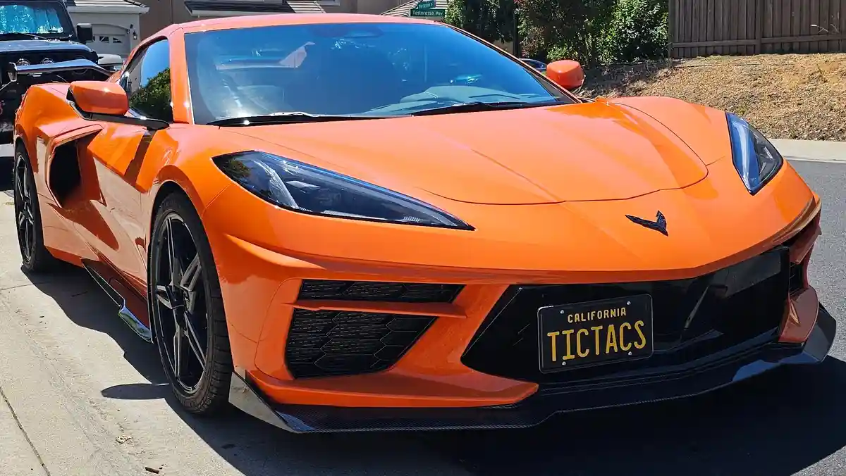 A bright orange Chevrolet Corvette sports car is parked on a residential street, its front grille and headlights prominent…