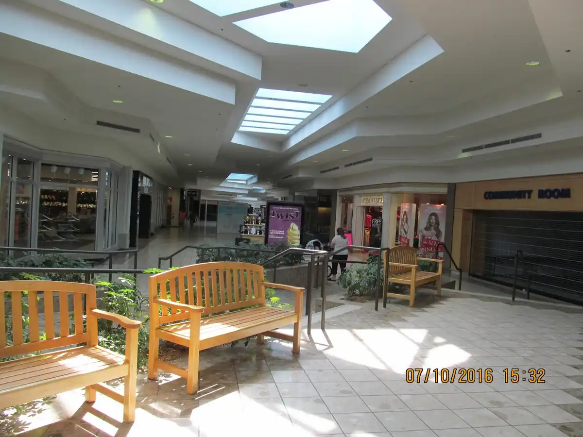 An empty indoor shopping mall corridor with wooden benches, skylights, and storefronts, including a closed 'COMMUNITY ROOM'…