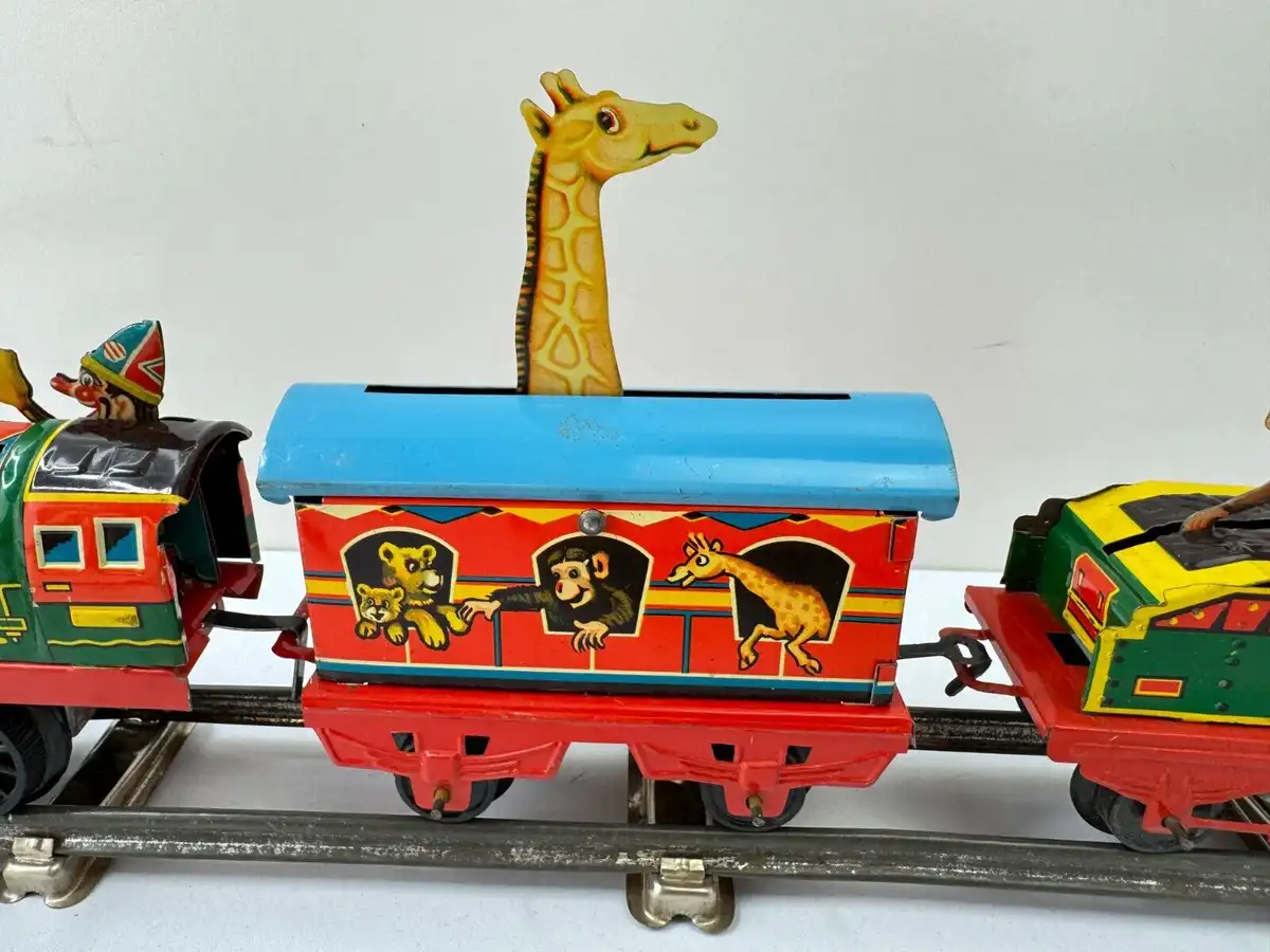A vintage tin toy train with a red and blue car featuring painted animals including a monkey, two cubs, and a giraffe. A…