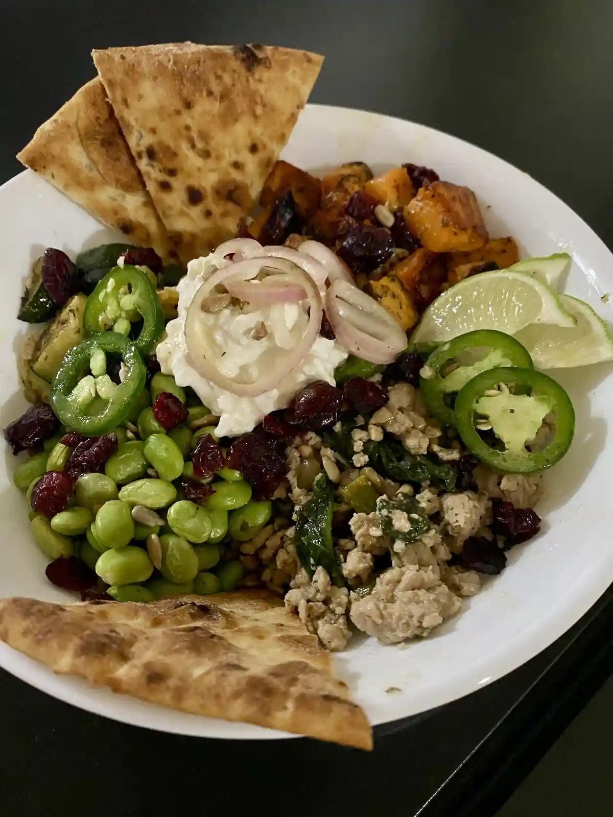 A close-up photo of a colorful, healthy-looking grain bowl in a white ceramic bowl, featuring sections of cooked edamame…