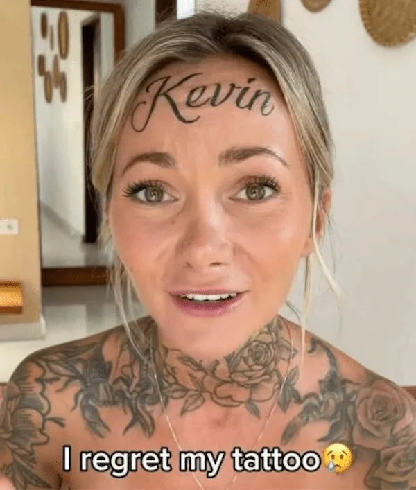 A woman with extensive tattoos on her neck and shoulders has the name 'Kevin' written in cursive script across her forehead…