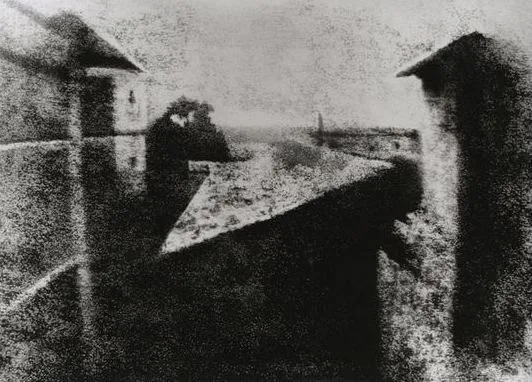 A grainy, black-and-white photo shows a blurry, shadowy figure sitting on a rooftop ledge, appearing ghostly and indistinct…