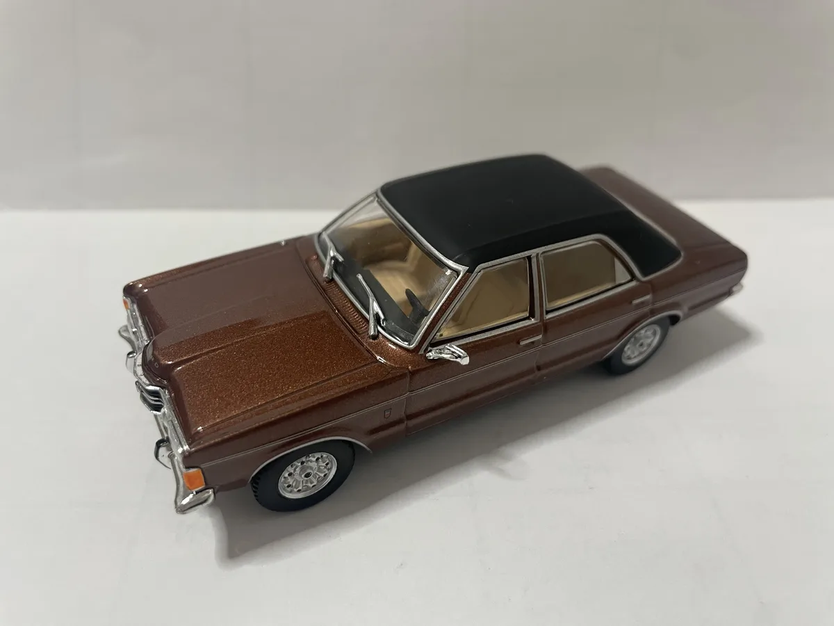 A brown die-cast model of a classic American sedan with a black roof, chrome trim, and detailed interior, photographed on a…