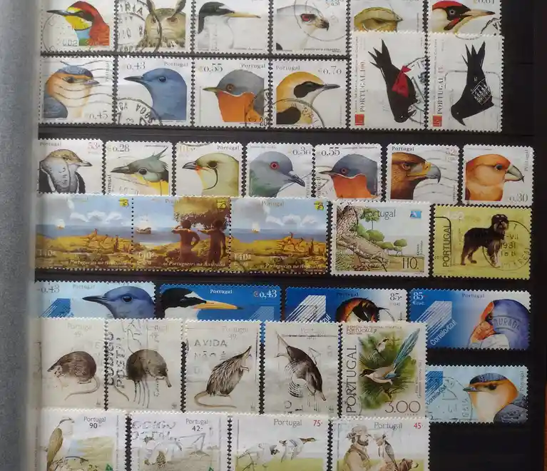 A collection of Portuguese postage stamps arranged in rows, featuring various birds, animals, and scenes, with some stamps…