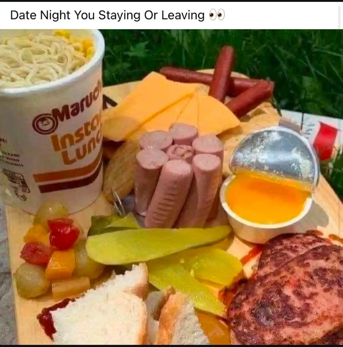 A wooden platter holds a chaotic assortment of low-quality food items including a cup of Maruchan instant lunch, hot dogs…