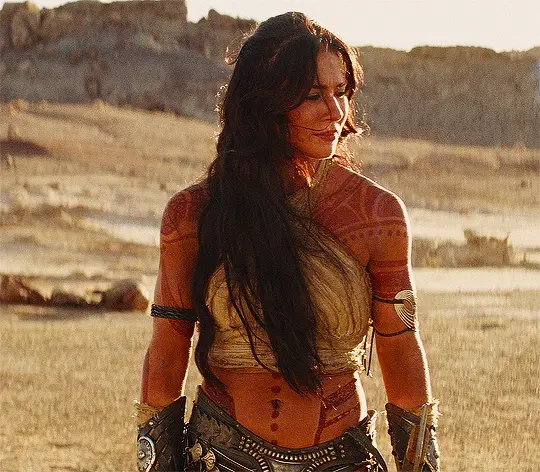 The image shows six panels of actress Megan Fox in a desert setting, wearing tribal-style armor and tattoos. The top three…