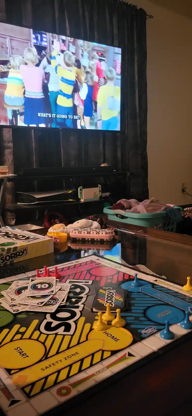 A 'Sorry!' board game is set up on a table in front of a TV showing a scene from 'The Wonder Years' where characters are…