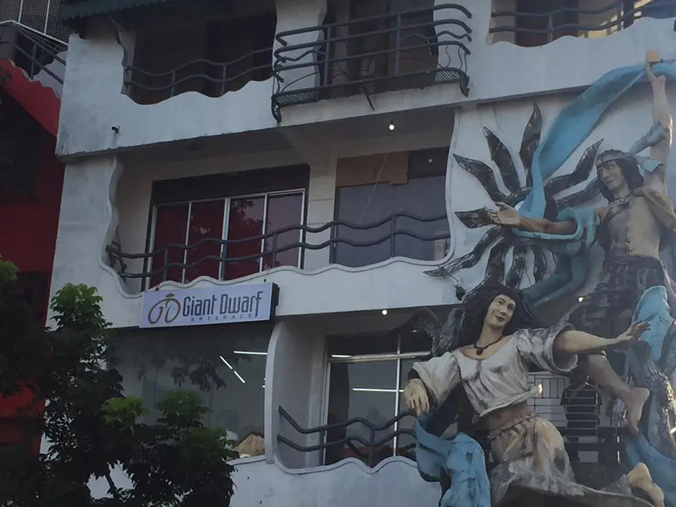 A building with a large, colorful mural of two figures in flowing robes, one appearing to be a giant and the other a dwarf…