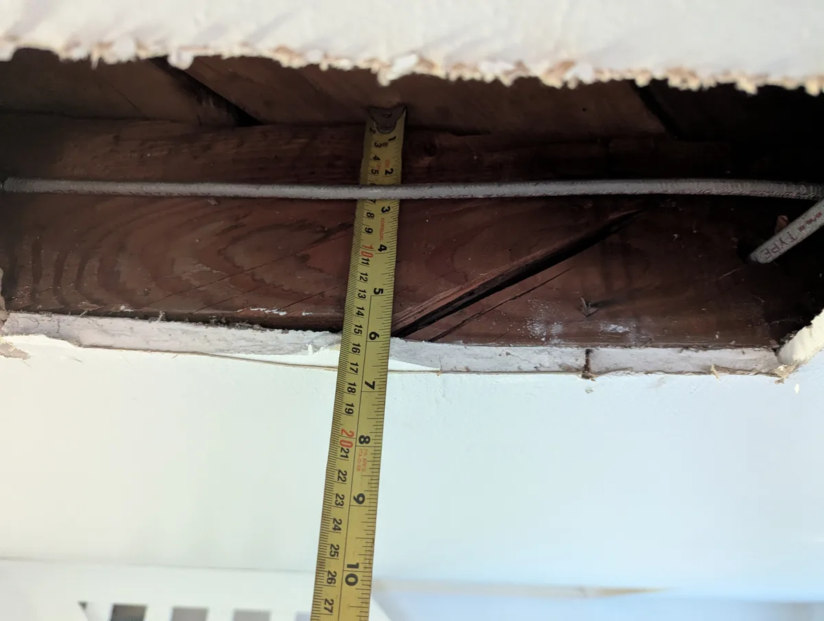 A yellow measuring tape is stuck vertically between a damaged ceiling and floor, showing a gap of about 20 inches. The…