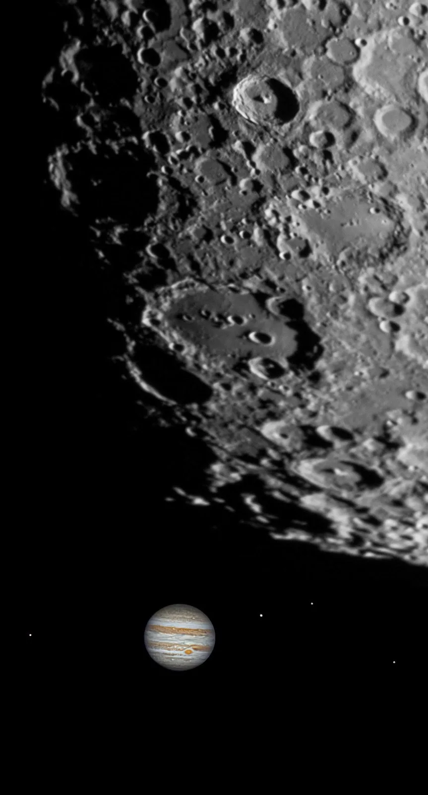 A black-and-white image shows the heavily cratered, rocky surface of a moon, likely Io or Europa, dominating the frame. In…