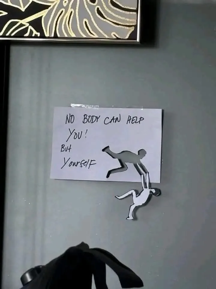 A handwritten note taped to a gray surface reads 'NO BODY CAN HELP YOU! But Yourself,' accompanied by two paper cutouts of…