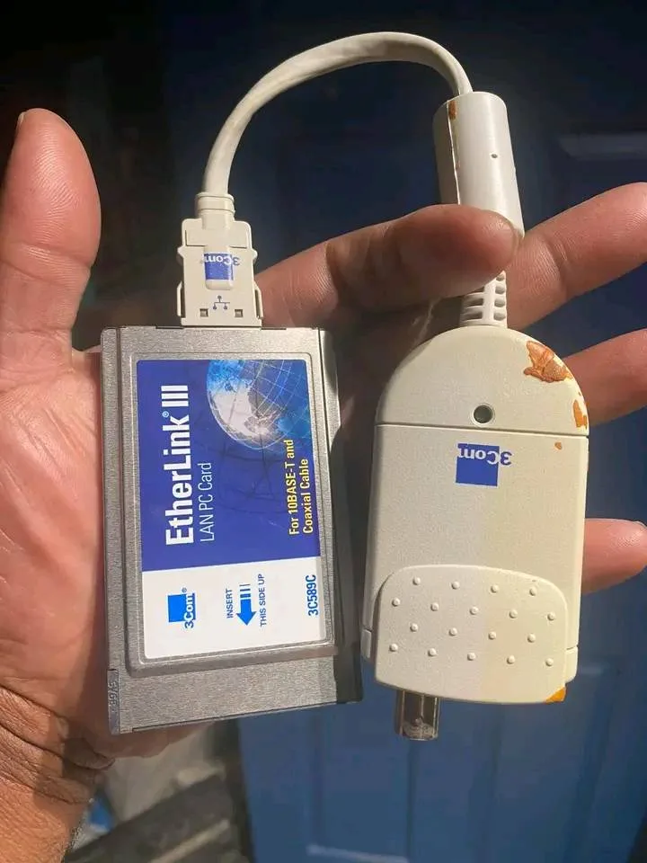 A hand holds two 3Com networking devices: a silver EtherLink III LAN PC Card with a blue label and a beige 3Com 10BASE-T and…