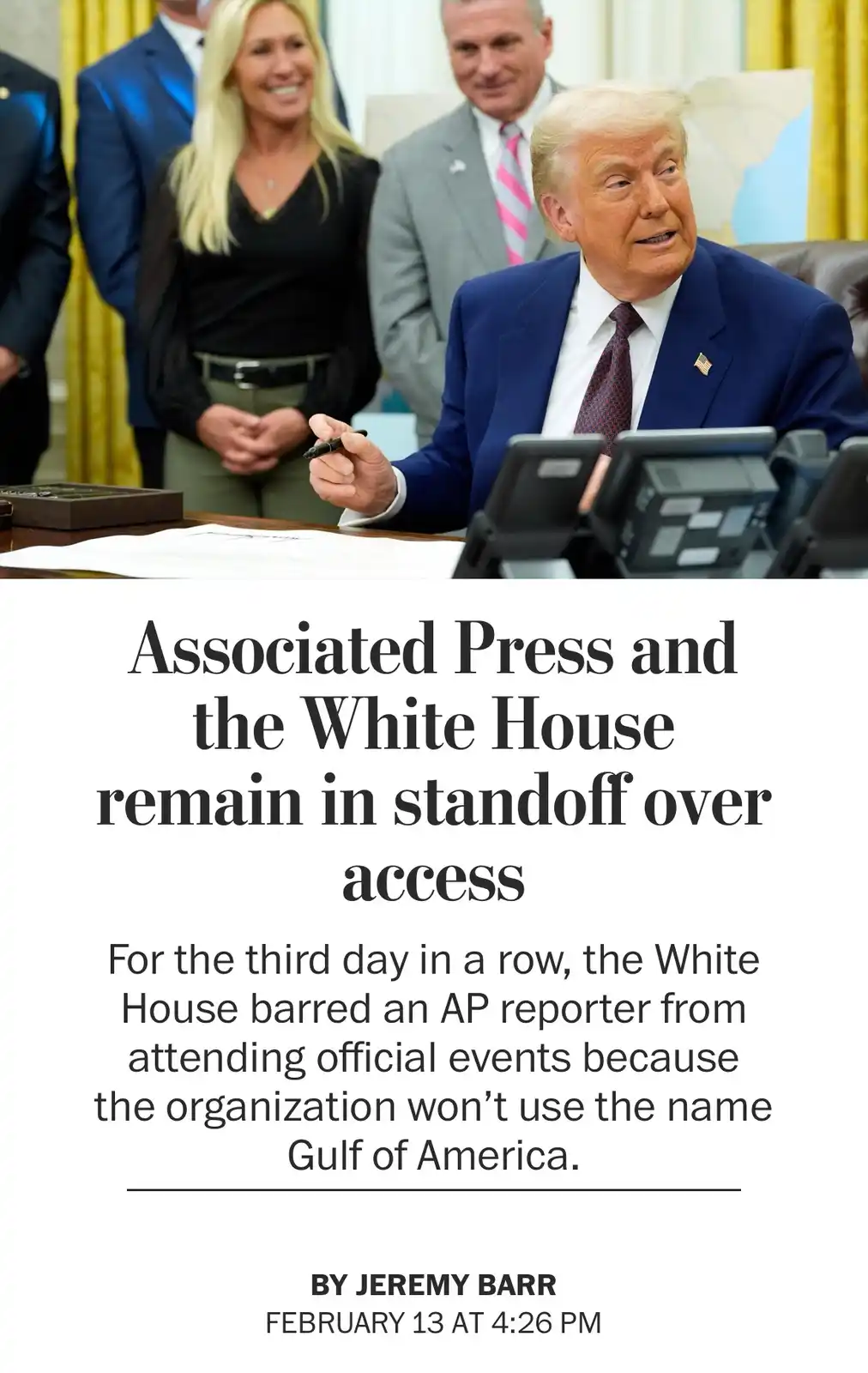 The image shows Donald Trump seated at a desk in what appears to be the Oval Office, holding a pen, with several people…
