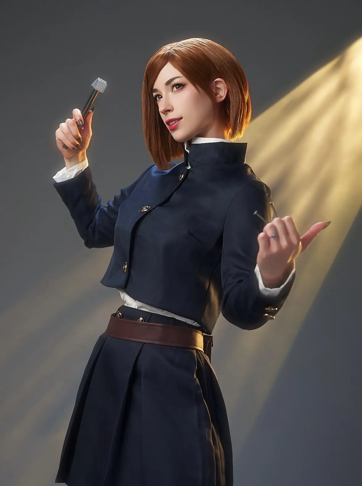A person in a dark blue school uniform with a white collar and brown belt holds a small hammer in one hand and a nail in the…
