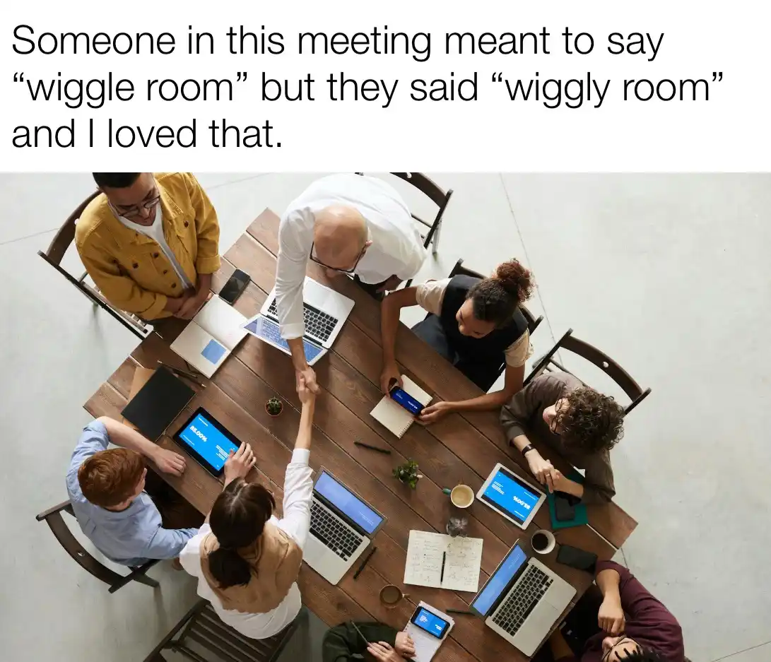 An overhead shot of six diverse people gathered around a wooden conference table, engaged in a meeting with laptops…