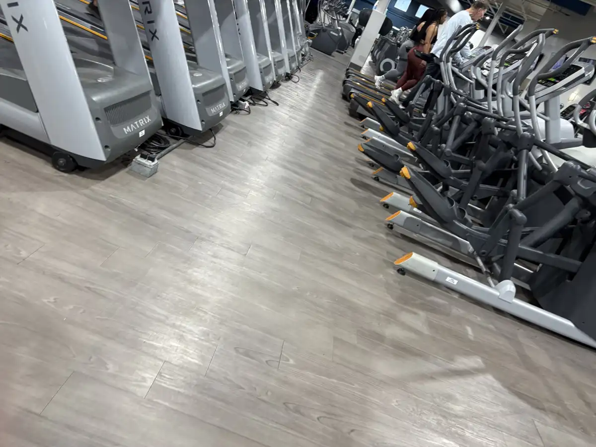 A low-angle shot of a gym floor with rows of unused treadmills on the left and folded elliptical machines on the right, with…