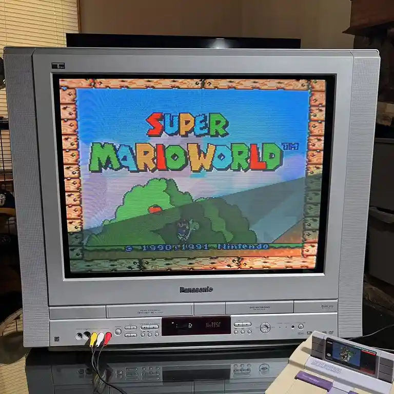 A silver Panasonic CRT television displays the title screen of Super Mario World, featuring the game's colorful pixelated…