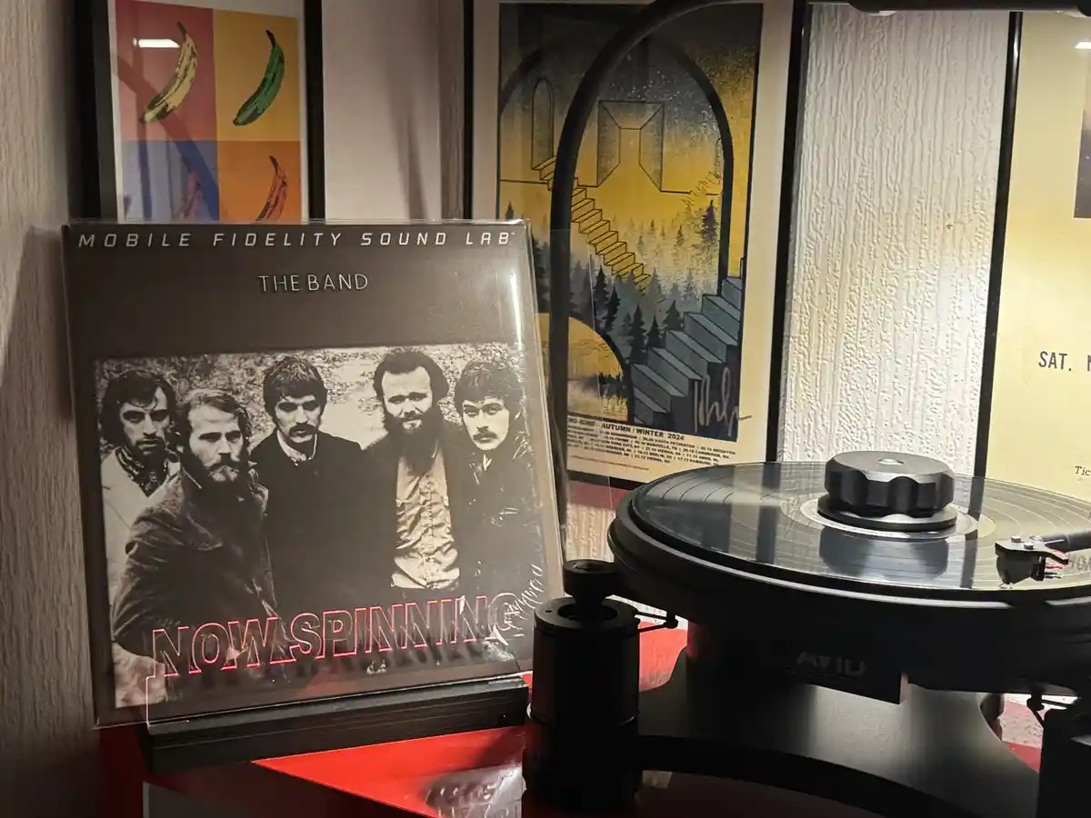 A vinyl record player sits next to a 'Mobile Fidelity Sound Lab' album of 'The Band', with the text 'NOW SPINNING' overlaid…