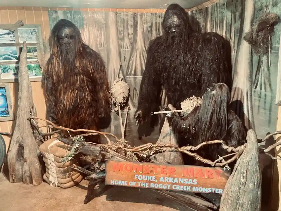 A museum diorama displays three large, hairy, ape-like creature figures standing in a swampy setting with wooden props and a…