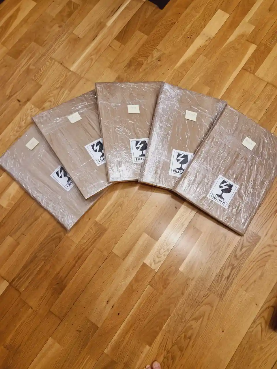 Four cardboard boxes wrapped in clear plastic sit on a wooden floor, each labeled with a 'FRAGILE' sticker and a small…