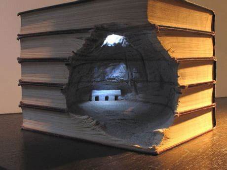 A large, thick book with a rough, excavated hole cut through its center, revealing a miniature cave interior with a small…