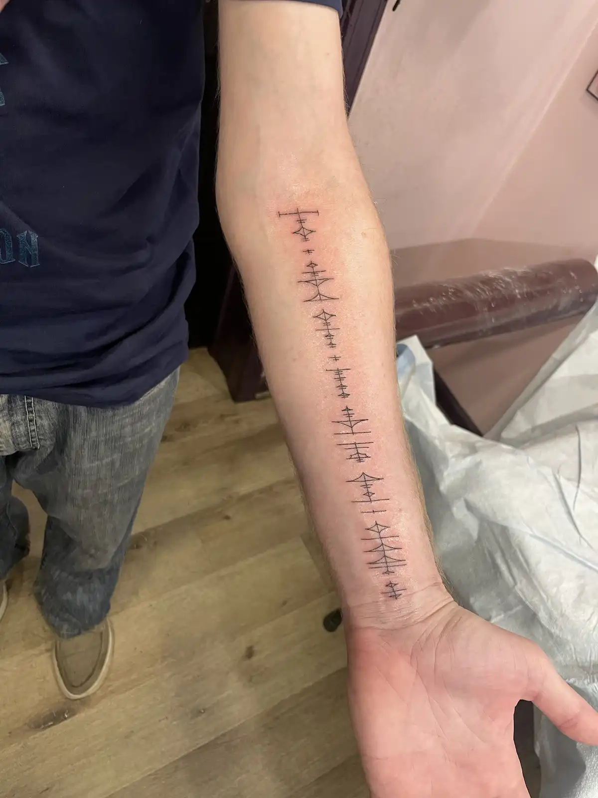 A person's forearm displays a vertical tattoo of stylized, geometric symbols resembling those from 'The Legend of Zelda…