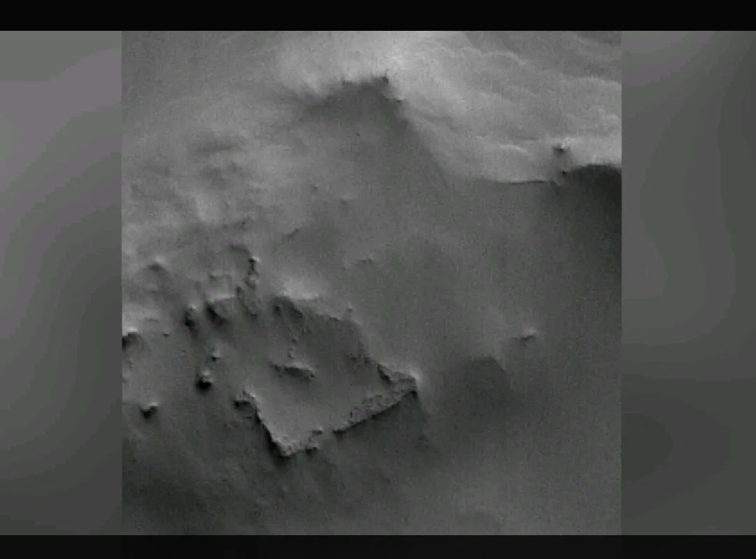 a grayscale, grainy image of a rocky, uneven surface resembling Martian terrain, with a large, irregularly shaped rock…