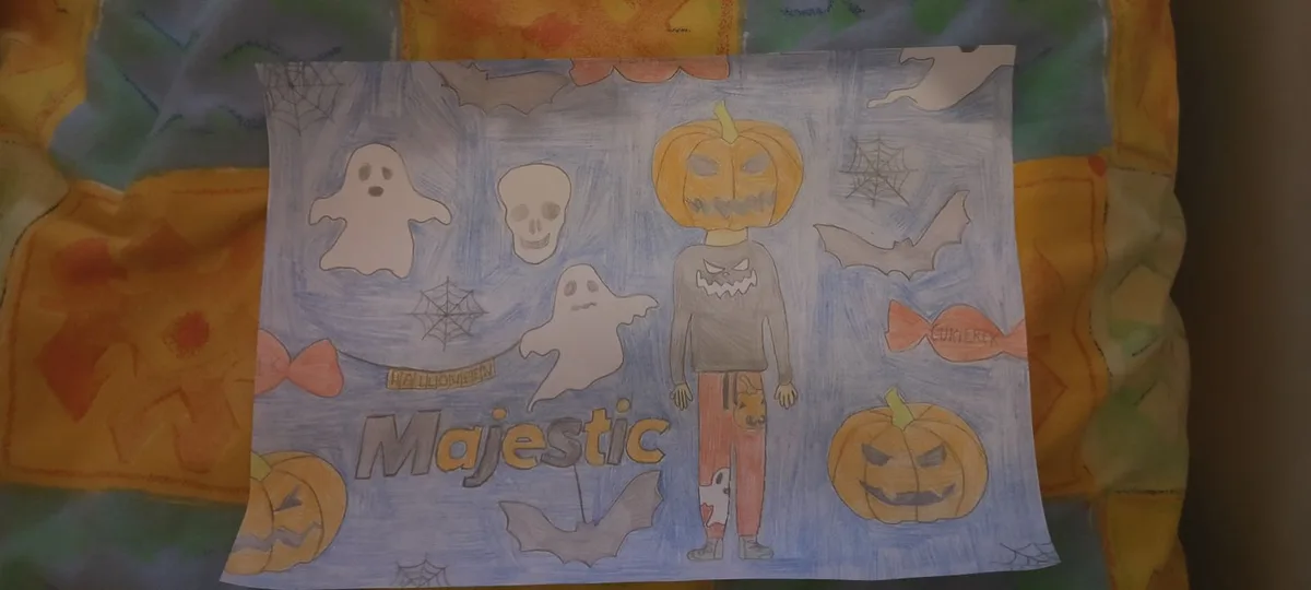 A child's Halloween drawing on blue paper shows a figure with a pumpkin head wearing a jack-o'-lantern shirt and pants…