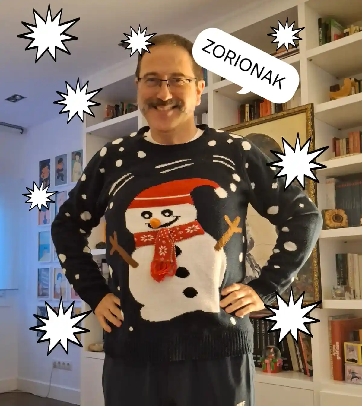 A man with glasses and a mustache smiles while wearing a festive black sweater featuring a large snowman with a red hat and…