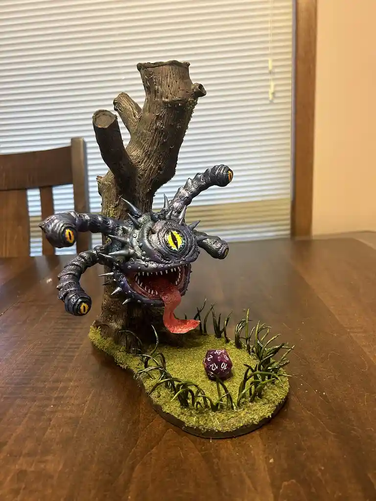 A painted miniature tree monster with a large central eye, multiple smaller eyes on its limbs, and a long tongue, emerging…