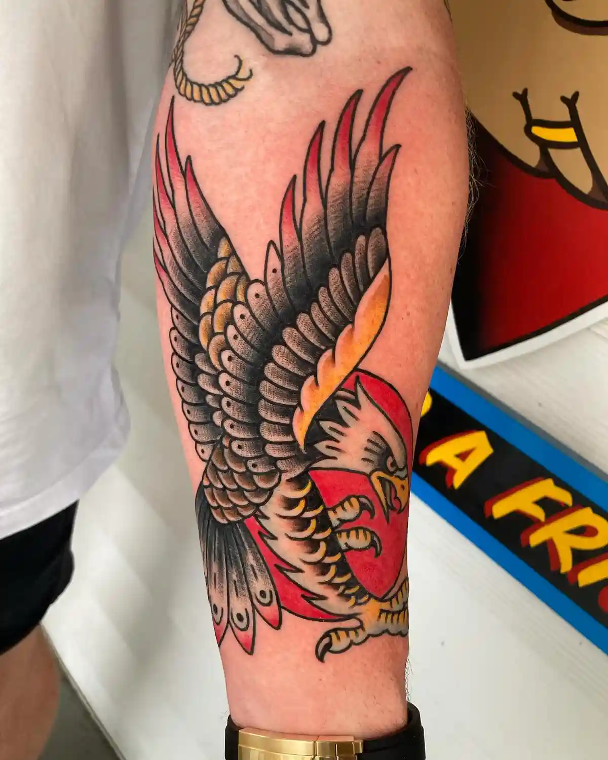 A close-up photo shows a person's forearm with a detailed tattoo of a stylized eagle with outstretched wings, rendered in…