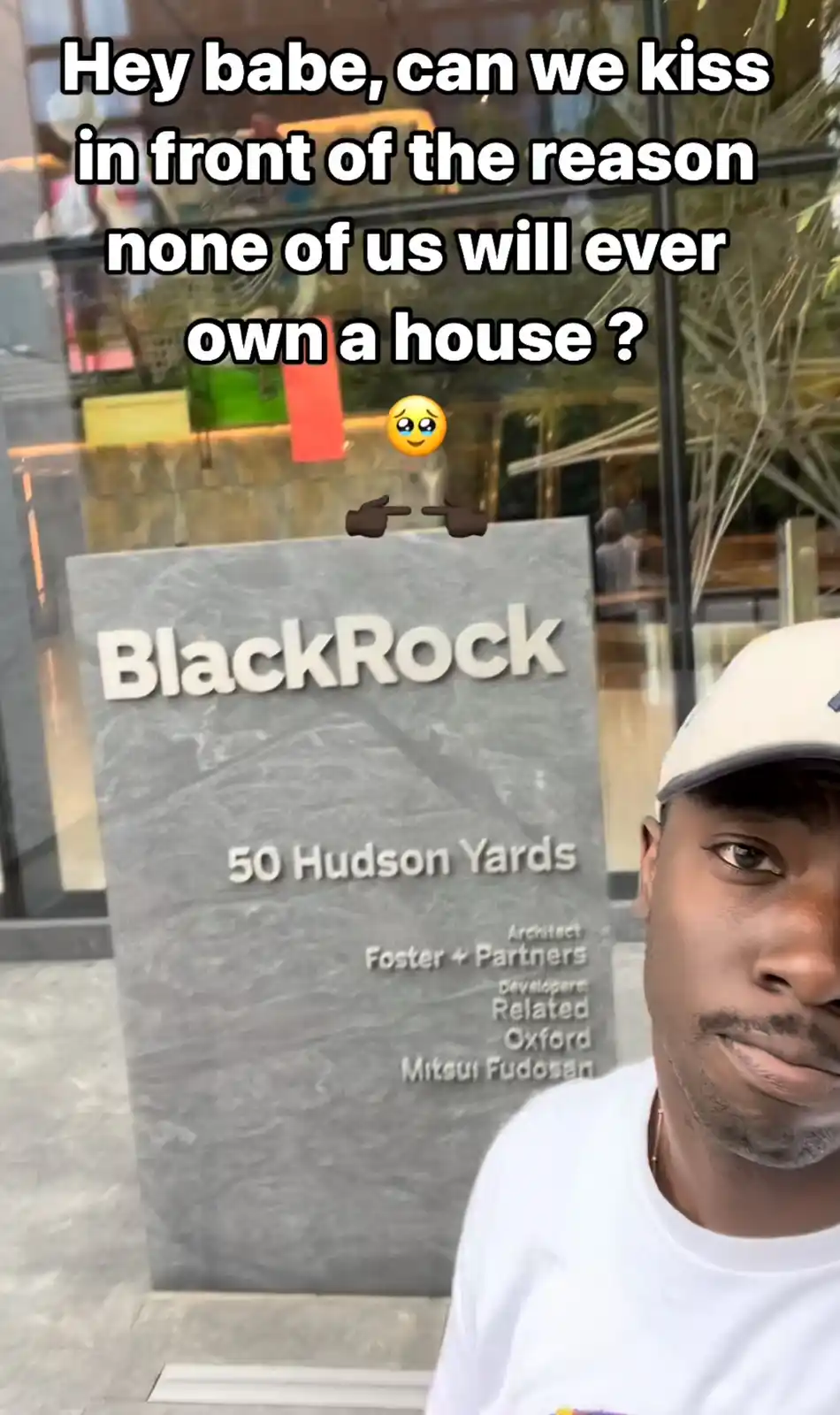 A man in a white t-shirt and cap stands in front of a large stone sign that reads 'BlackRock 50 Hudson Yards' with architect…