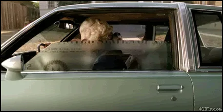 A sequence of six panels shows a person with a large white wig sitting inside a car, viewed through the window. The car…