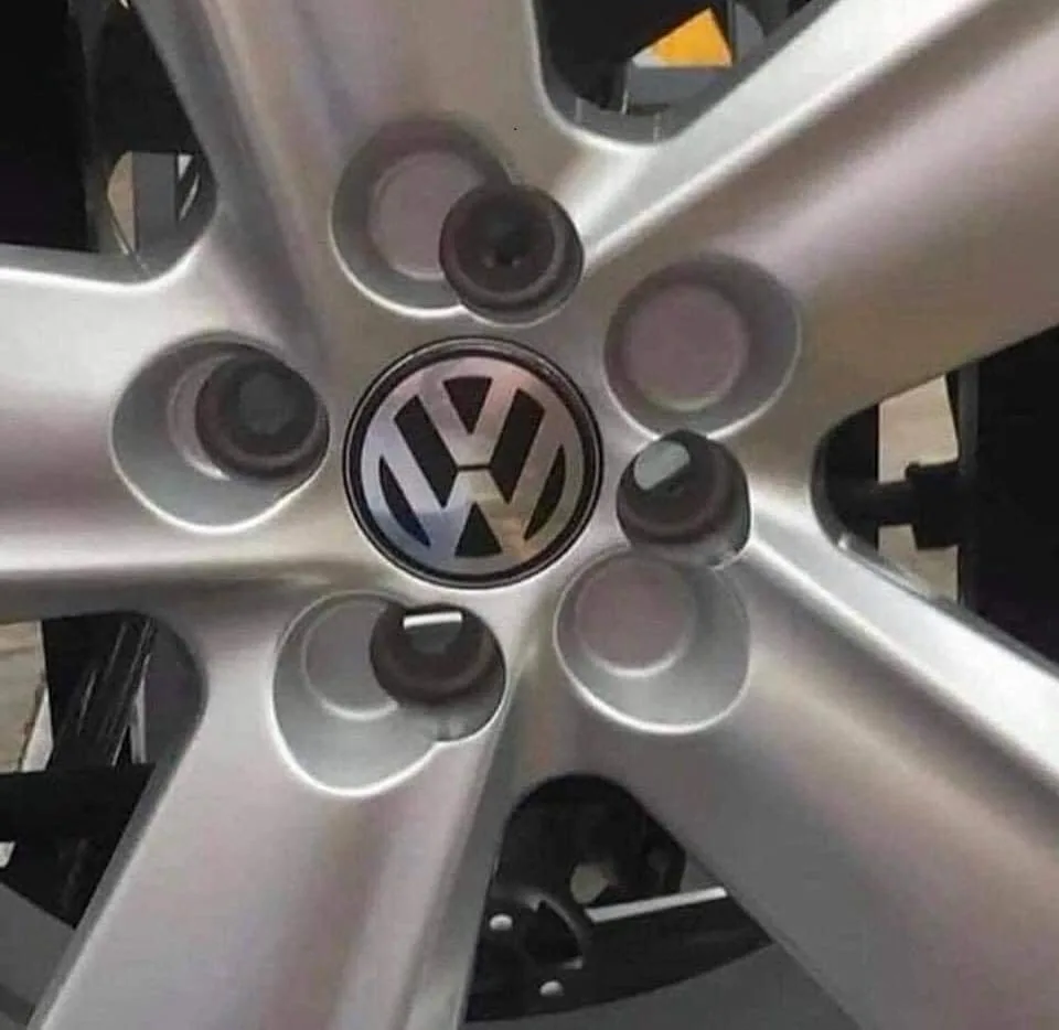 A close-up of a silver Volkswagen car wheel showing the VW logo in the center, with five lug nuts visible around it. The…