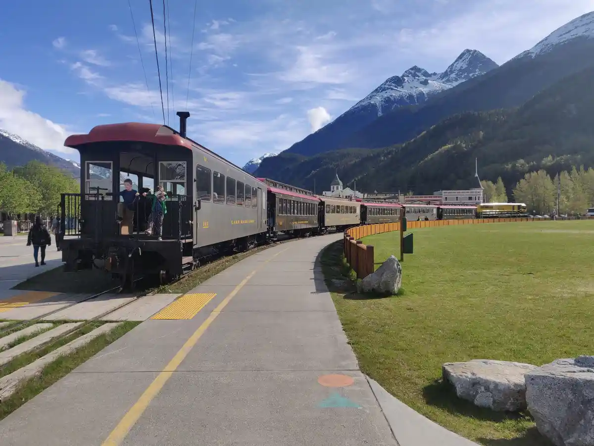 A scenic photo of a vintage train with children on its front platform, set against snow-capped mountains and a clear blue…