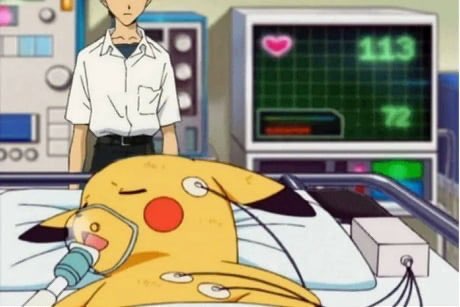 A yellow cartoon Pokémon, Pikachu, lies in a hospital bed with an oxygen mask over its mouth and nose, connected to medical…