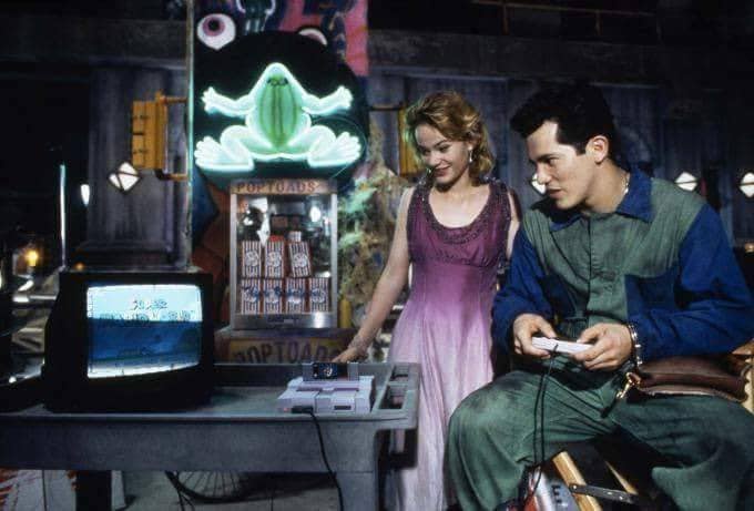 A man and woman are in a dimly lit arcade, the man is focused on playing a video game on a vintage console while the woman…
