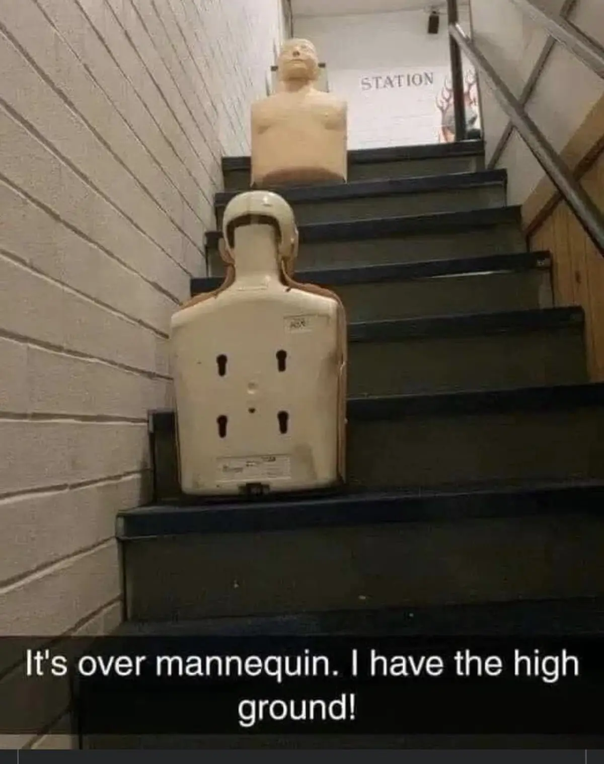 Two mannequins are positioned on a staircase, one at the bottom with its back to the camera showing a white torso with black…