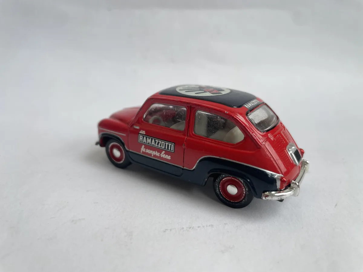 A red and black vintage toy car with 'un RAMAZZOTTI fa sempre bene' written on its side, sitting on a plain white surface…