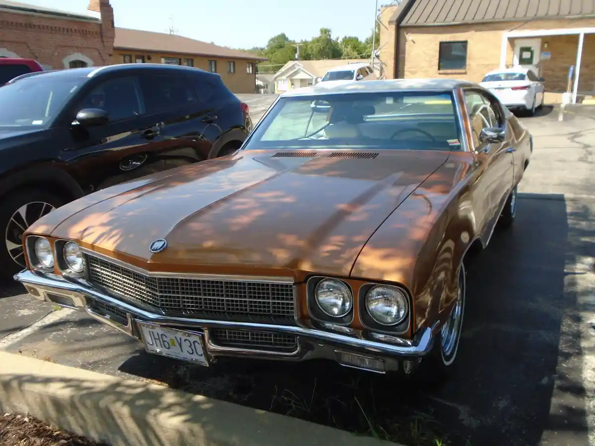 A shiny brown classic American muscle car, likely a Buick, is parked in a lot next to a modern black SUV. The car's Missouri…
