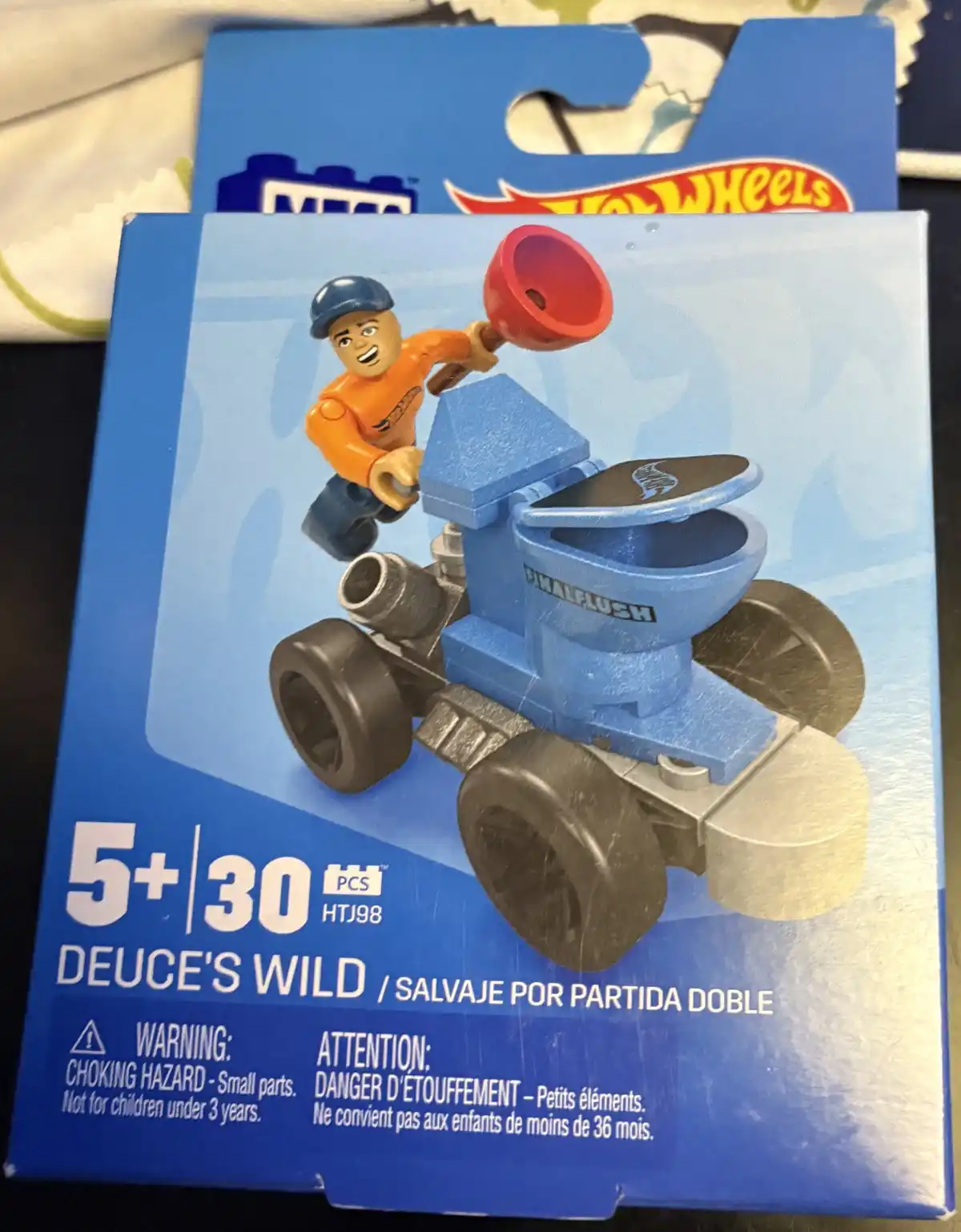 A Hot Wheels toy package shows a blue car shaped like a toilet with the word 'FINALFLUSH' on the side, driven by a…