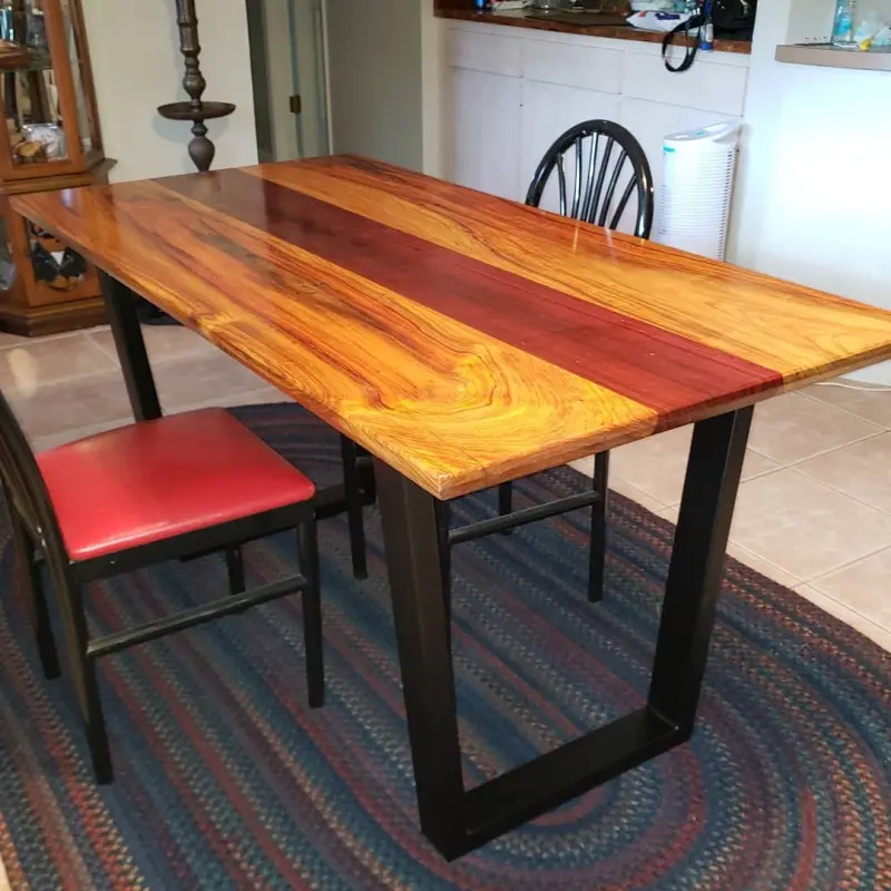 A photo of a custom-made wooden dining table with a striking two-tone finish—light amber wood on the sides and a bold, deep…