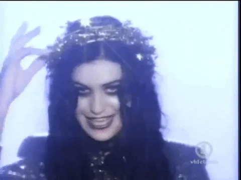 A six-panel image collage from a music video, showing a woman with dark hair and heavy makeup in various poses, including…
