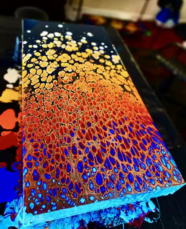 A close-up photo of a rectangular, glossy art piece with a vibrant, abstract pattern resembling a cosmic nebula or cellular…