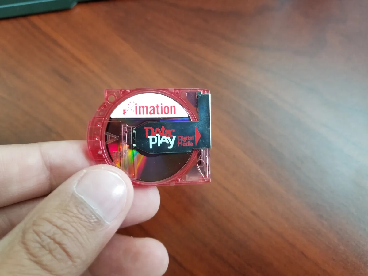 A hand holds a small, red, transparent plastic DataPlay digital media cartridge, branded with 'imation' and 'Data™ Digital…