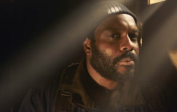 A man with a beard and beanie looks intensely at the camera with a serious, slightly annoyed expression. He wears a dark…
