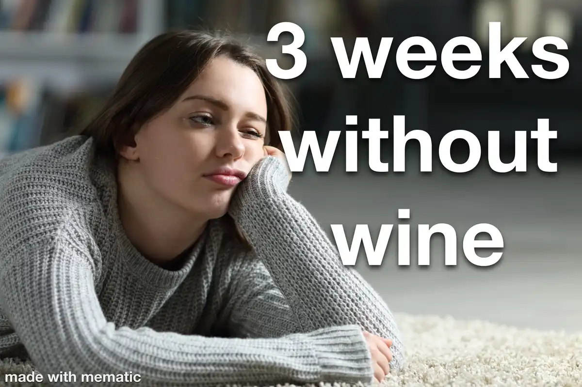 A woman in a gray knit sweater lies on a light-colored carpet, resting her head on her hand with a weary, pensive…
